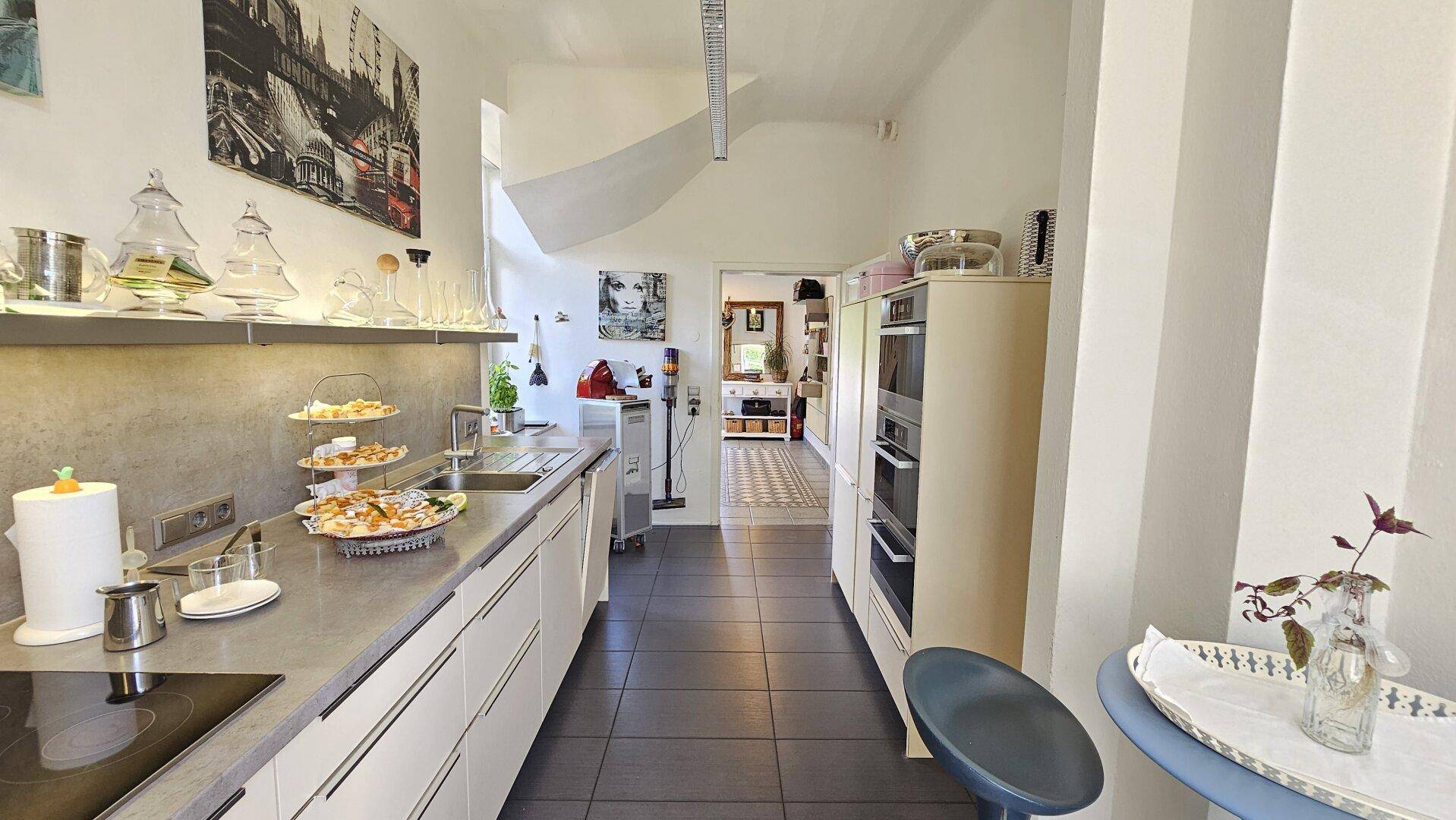 Moderne, helle Küche mit weißen Schränken, integrierten Geräten und dunklem Fliesenboden.