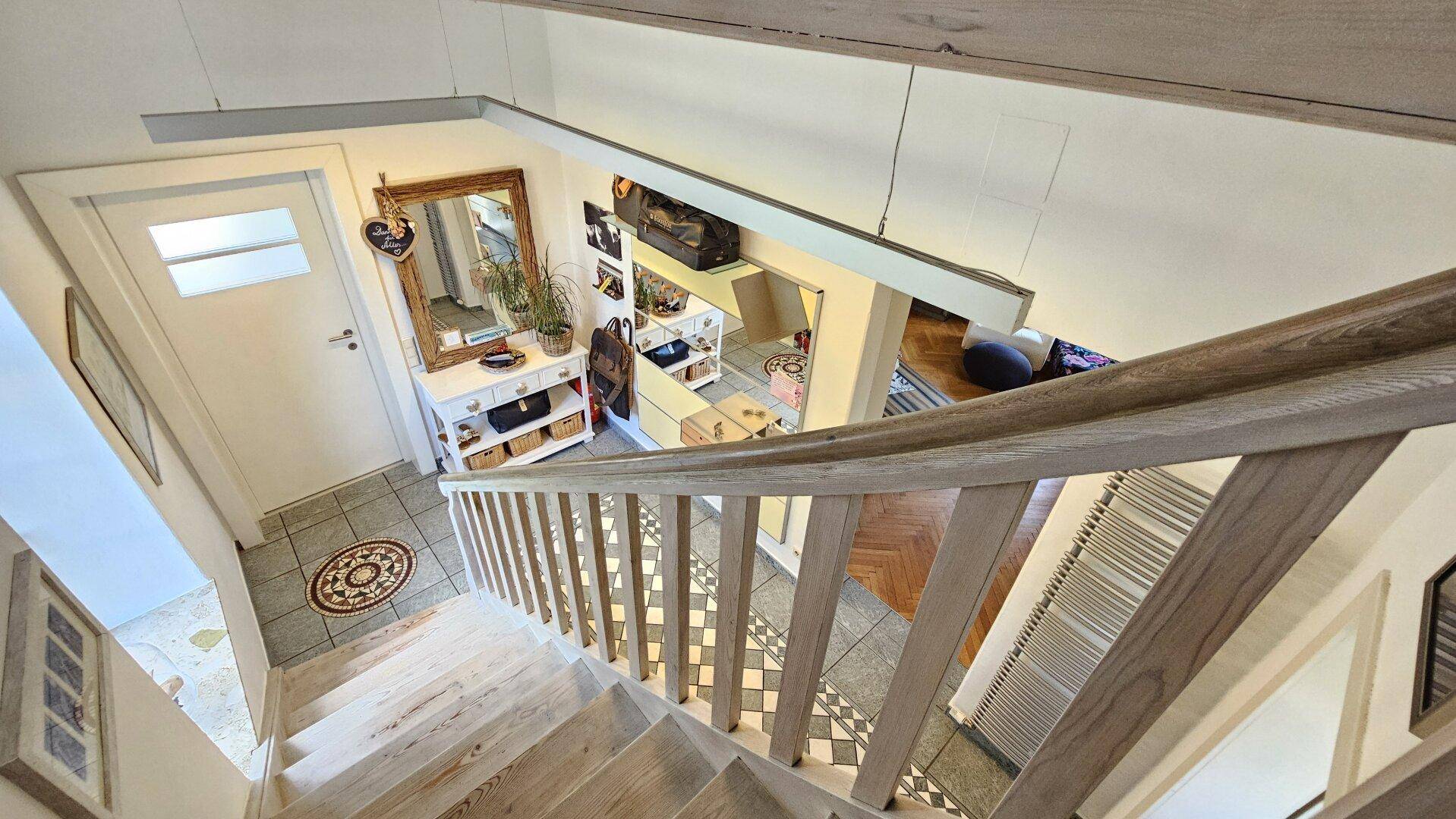 Blick von der Treppe in den Eingangsbereich mit Spiegel, Ablageflächen und gemustertem Boden.