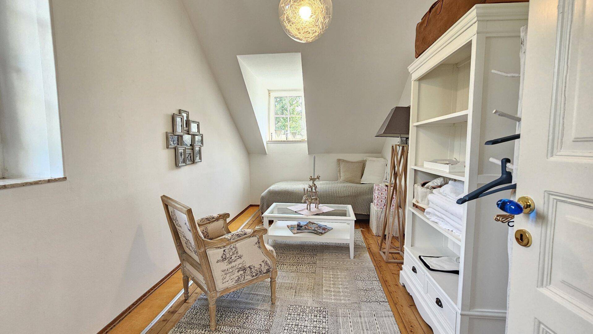 Gemütliches Zimmer mit Einzelbett, Lesesessel und Dachschräge, ideal als Gäste- oder Arbeitszimmer.