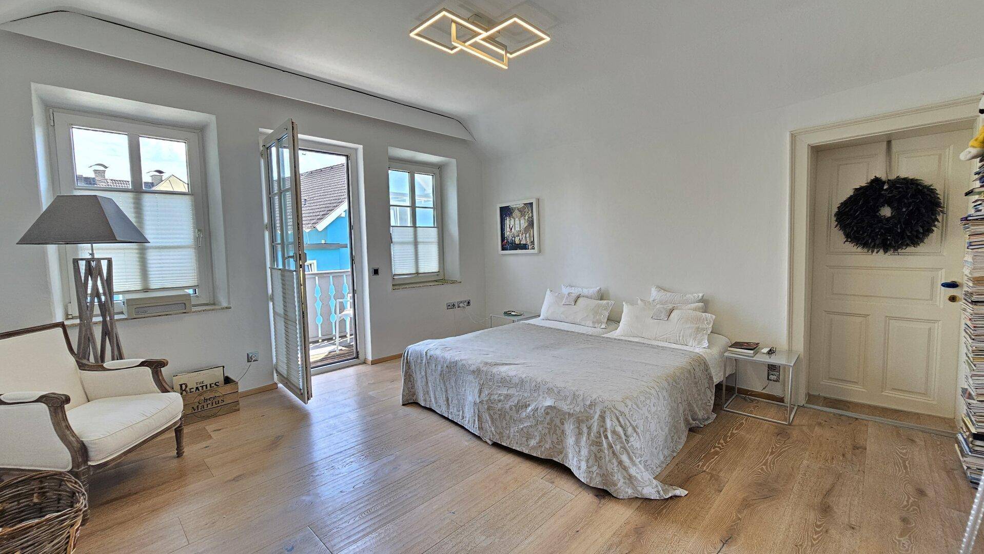 Helles Schlafzimmer mit Holzboden, Doppelbett und Zugang zu einem kleinen Balkon.