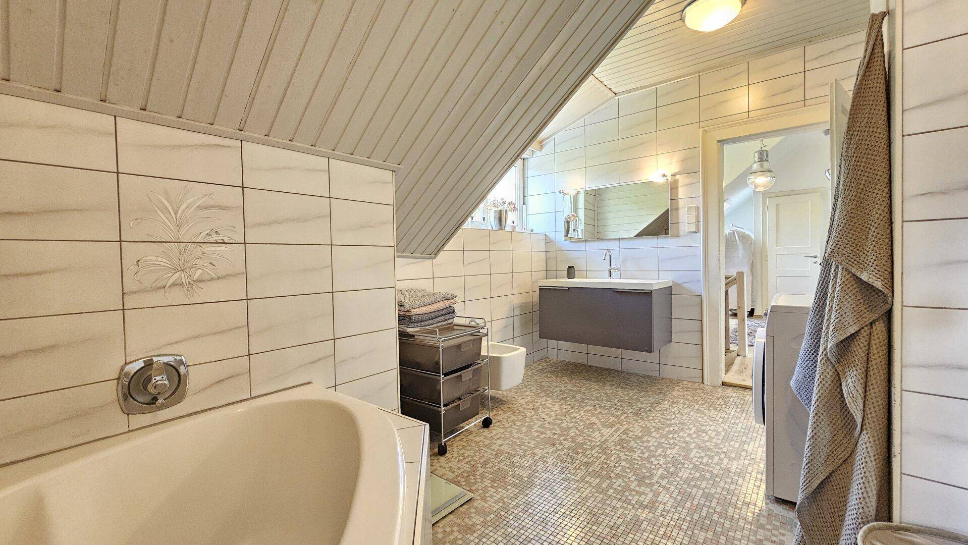 Badezimmer mit Badewanne, modernem Waschtisch, Fliesen und Dachschräge, hell und funktional.