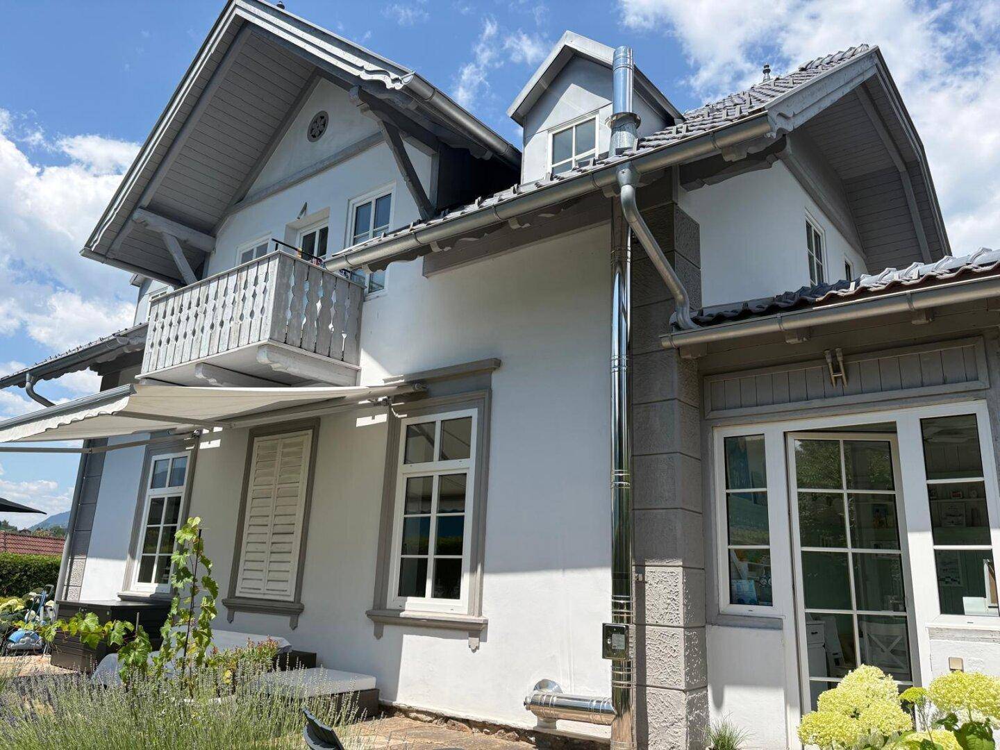Seitenansicht des Hauses mit Balkon, ausgefahrener Markise und einem modernen Edelstahlkamin.