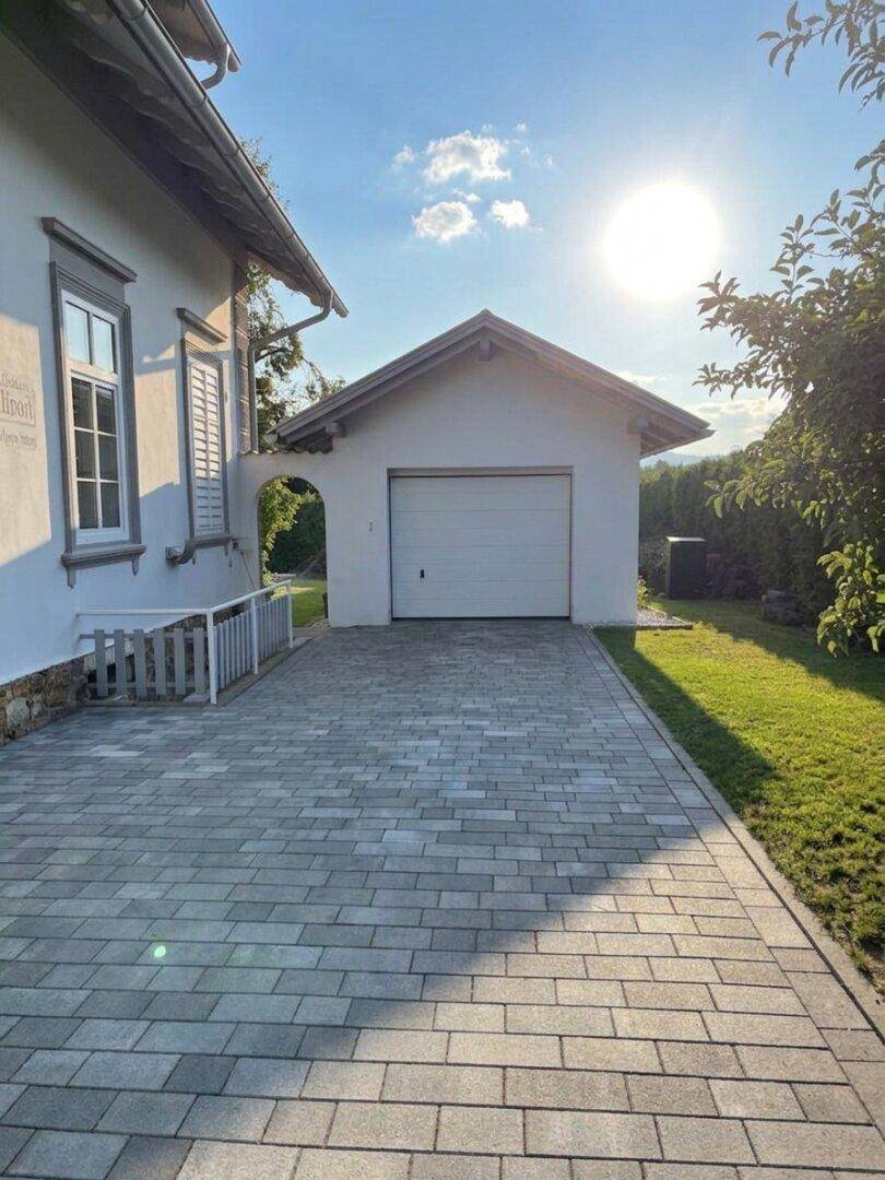 Geräumige Auffahrt mit Pflastersteinen, die zu einer freistehenden Garage führt, bei Sonnenschein.