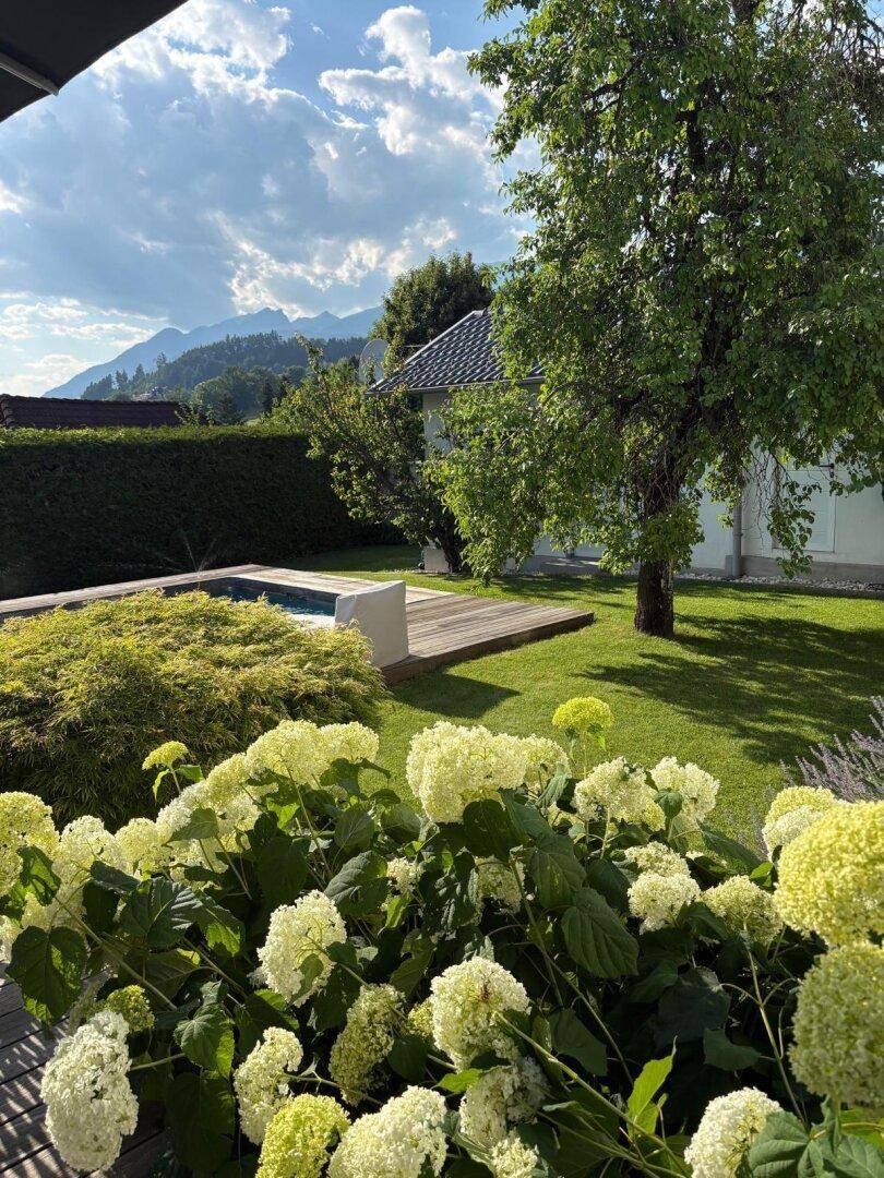 Gepflegter Garten mit kleinem Pool, Holzdeck und herrlichem Bergblick unter blauem Himmel.