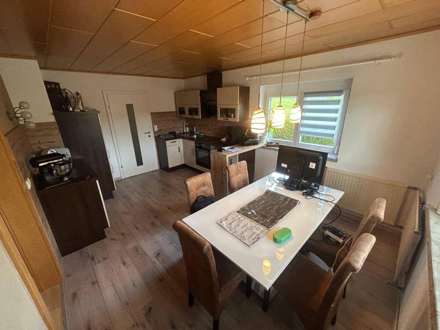 Offene Küche mit Holzboden, Holzdecke und Essbereich mit modernem Tisch.