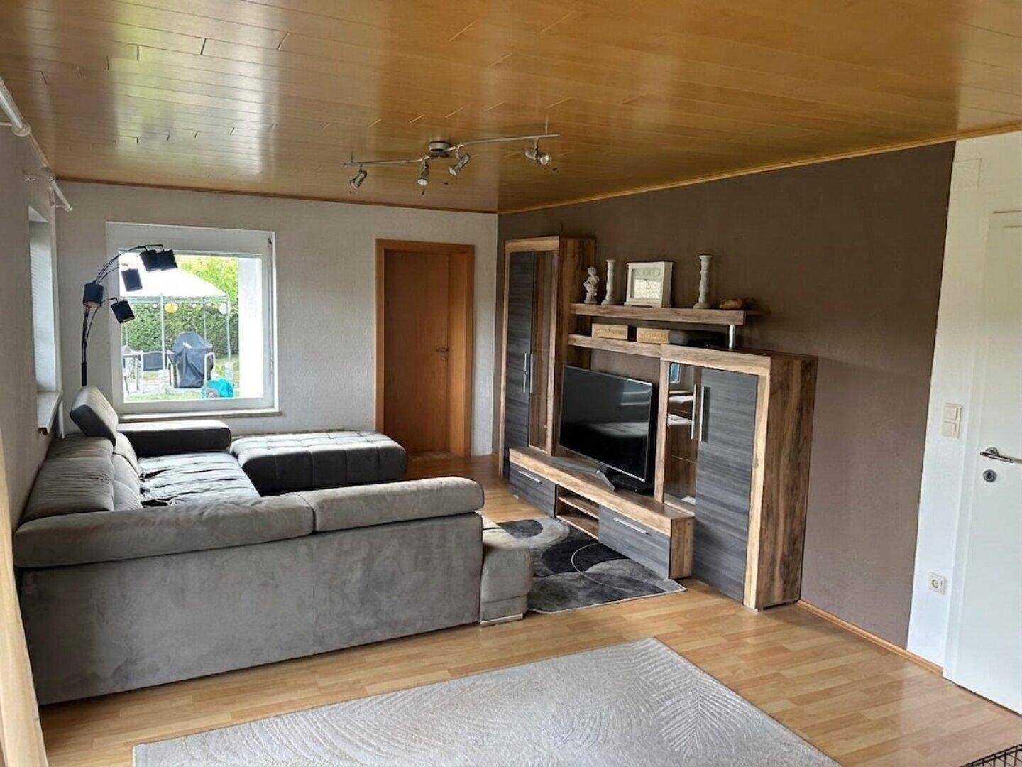 Gemütliches Wohnzimmer mit großem Ecksofa, TV-Möbel und Holzdecke.