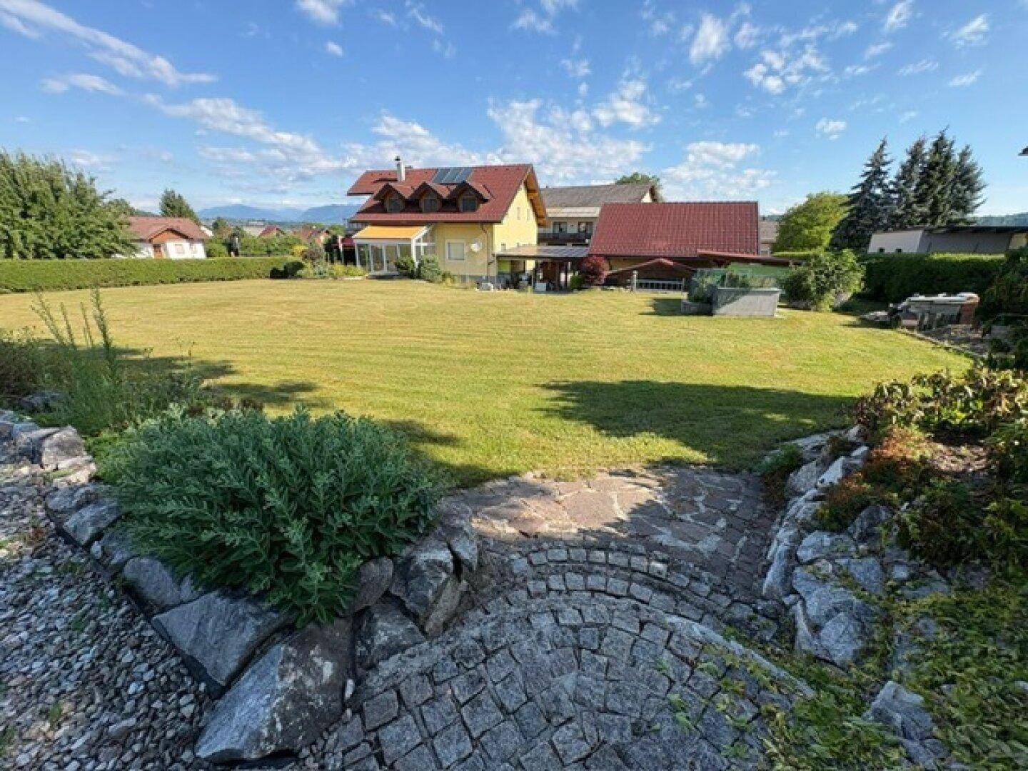 Weitläufiger Garten mit Rasenfläche, Steintreppe und Blick auf das Wohnhaus.