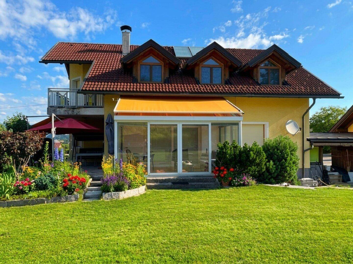 Rückseite des Hauses mit Wintergarten, Markise und blühendem Garten.