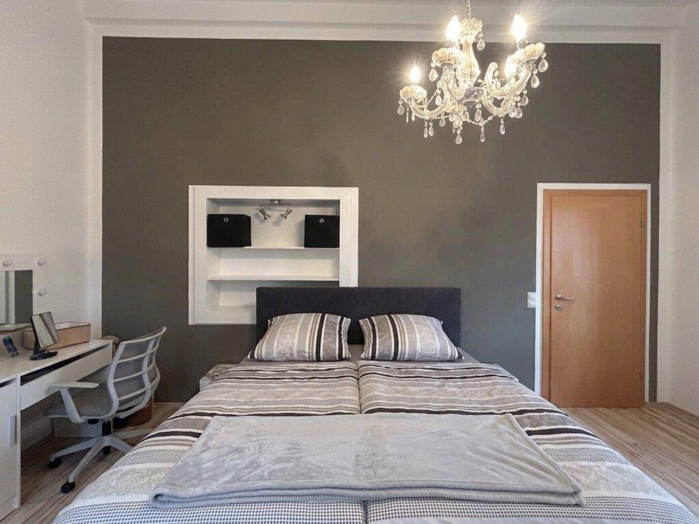 Schlafzimmer mit Doppelbett, Schreibtisch und elegantem Kronleuchter.