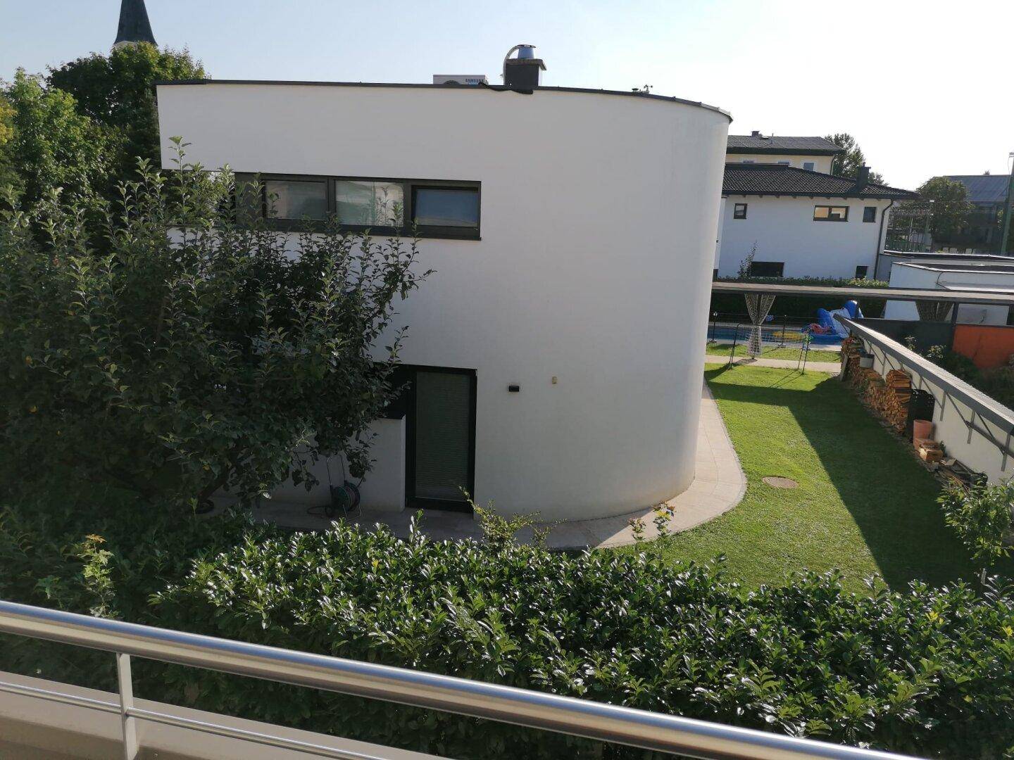 Moderne weiße Gebäudefassade mit geschwungener Form, umgeben von Rasen und Sträuchern.