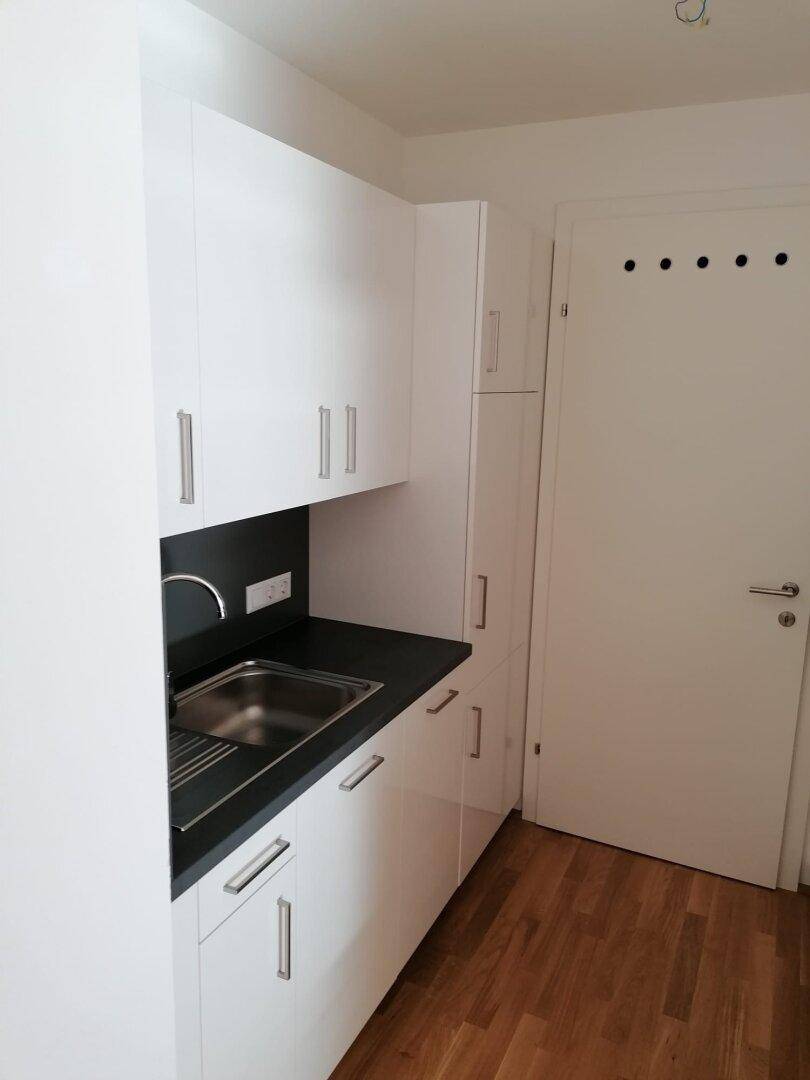 Kleine Küchenzeile mit weißen Schränken, Spüle und hellem Holzfußboden.