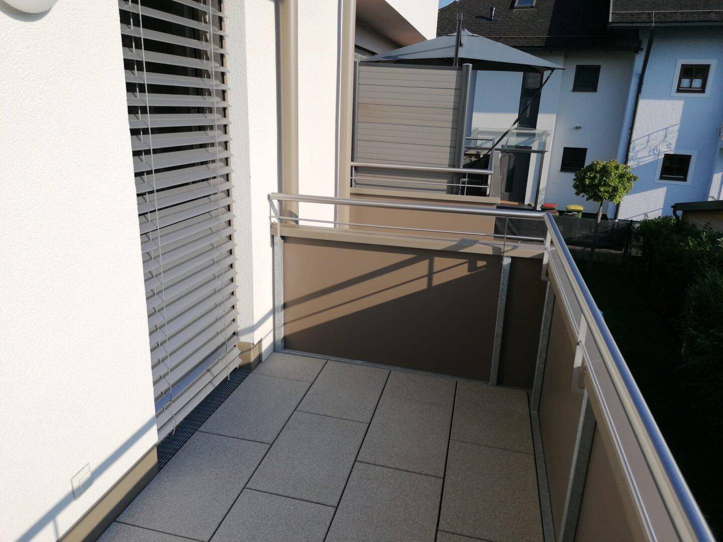 Detailansicht eines Balkons mit modernen Fliesen, Metallgeländer und Fenster mit Jalousien.