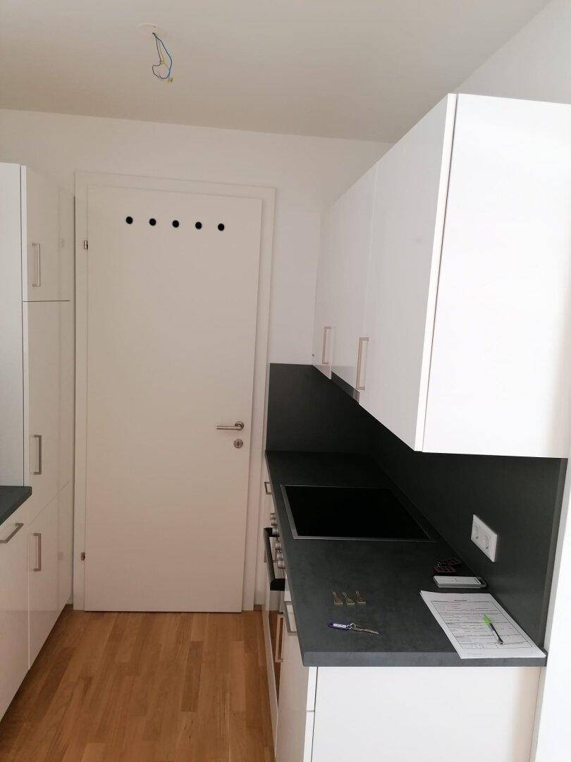 Küchenzeile mit weißen Oberschränken, dunkler Arbeitsplatte und Holzboden, neben einer Tür.