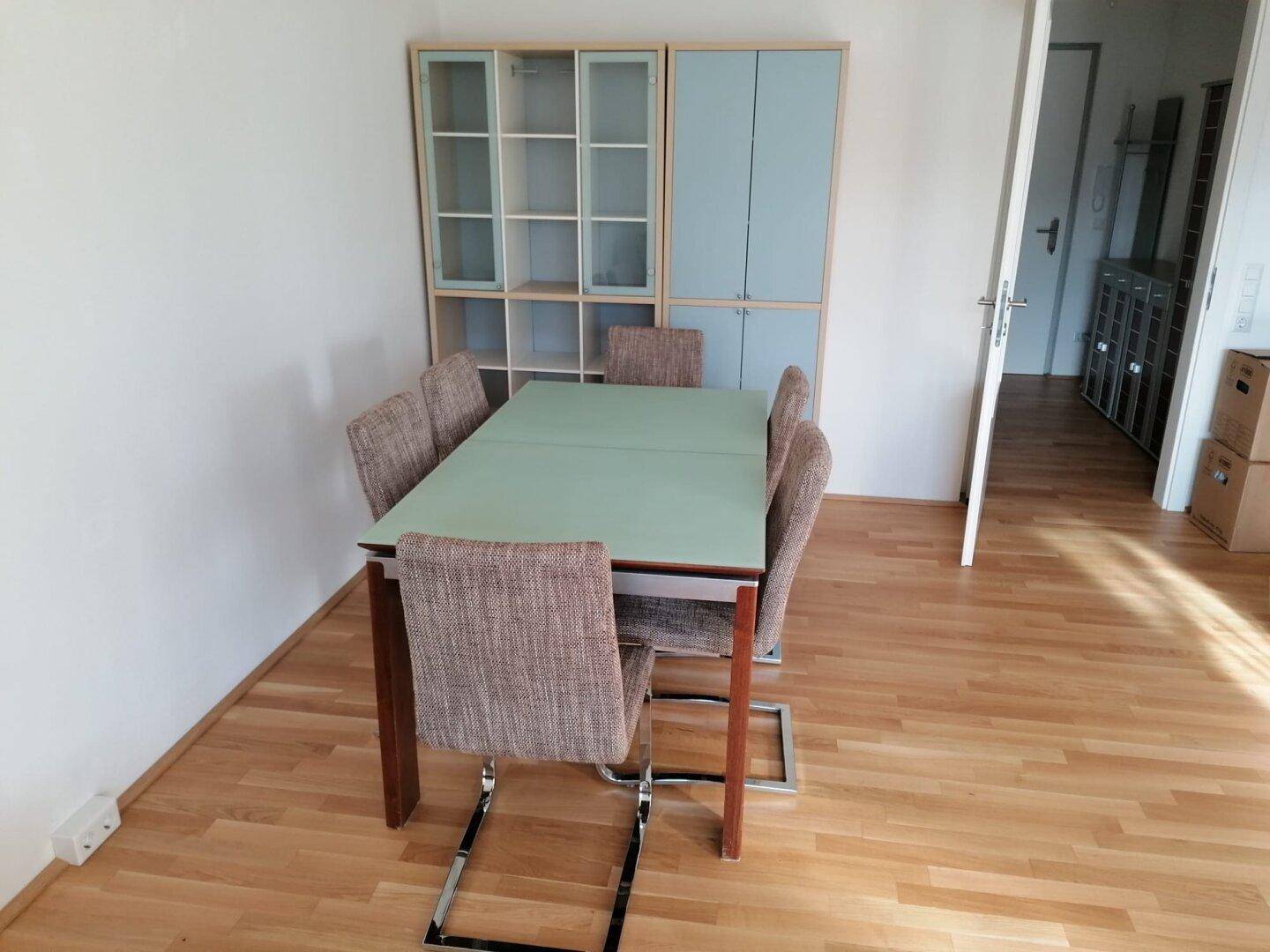 Essbereich mit Esstisch und Stühlen, hellem Holzboden und einem Schrank im Hintergrund.