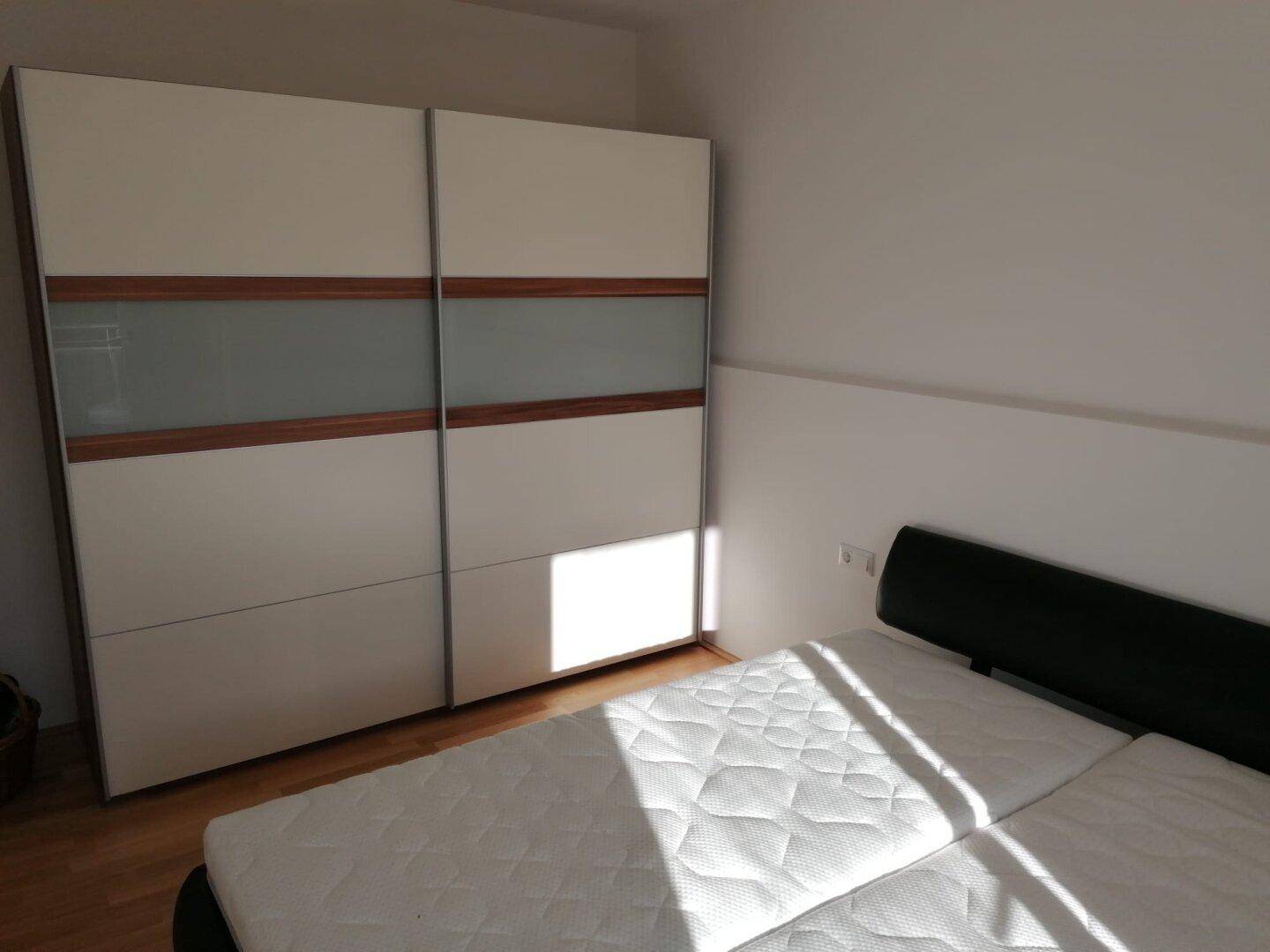 Schlafzimmer mit Doppelbett und großem Schiebetürenschrank auf hellem Holzfußboden.