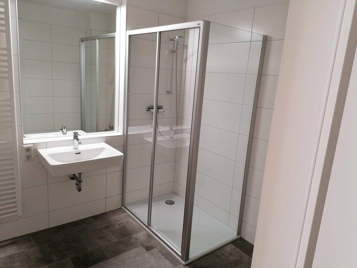 Modernes Badezimmer mit Duschkabine, wandhängendem Waschbecken und hellen Fliesen.