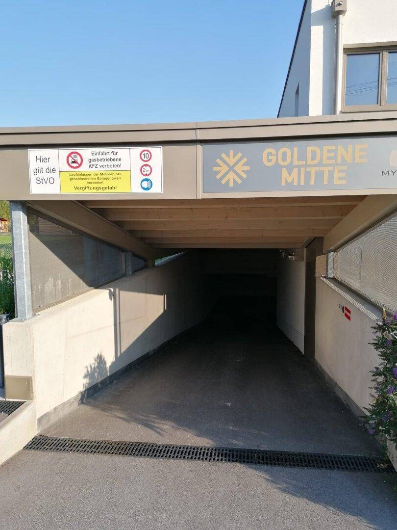 Einfahrt zu einer Tiefgarage mit Rampe und Hinweisschildern für die Bewohner.