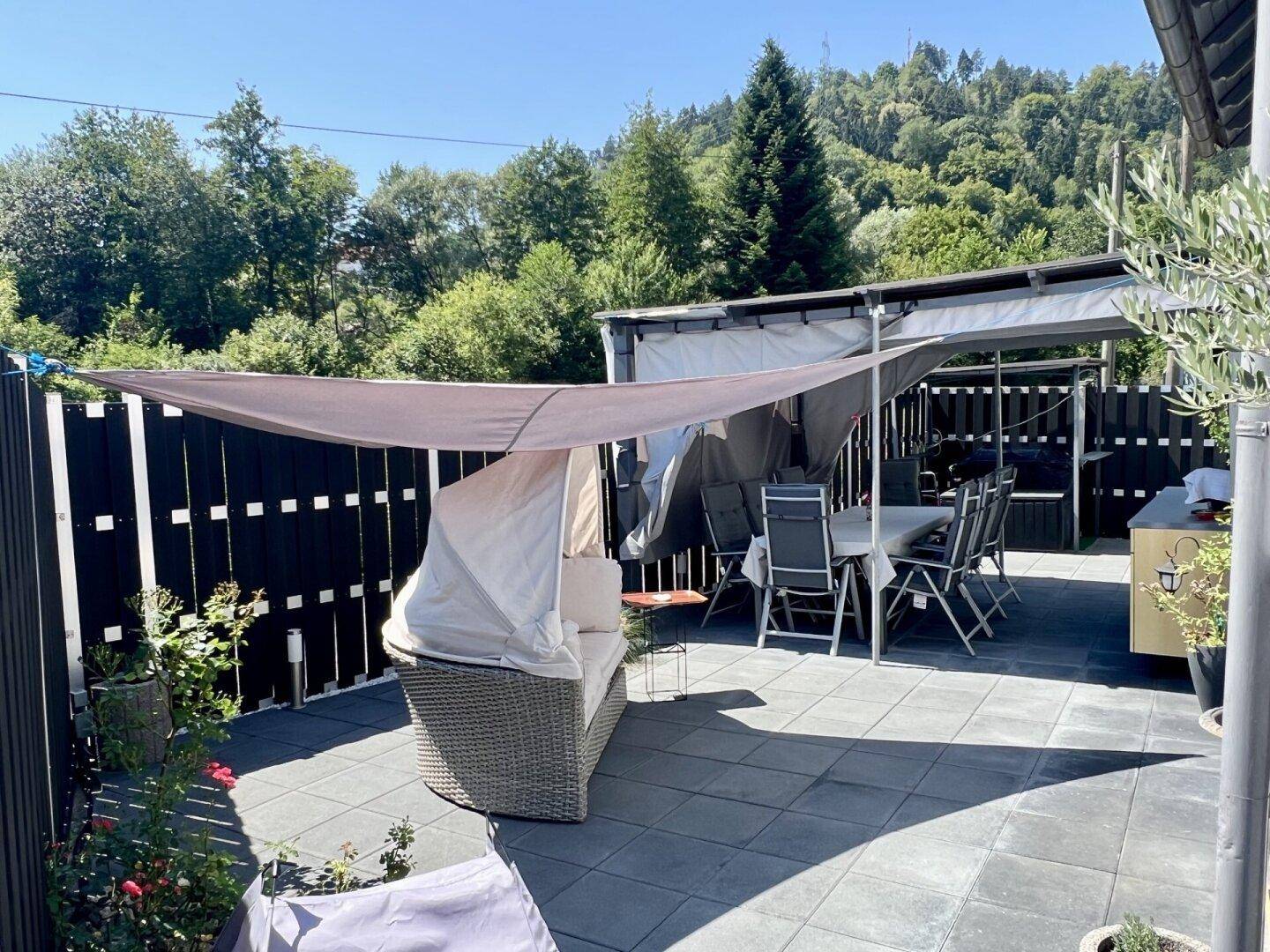 Gemütliche, überdachte Terrasse mit Essbereich und Lounge-Sofa, umgeben von Pflanzen.