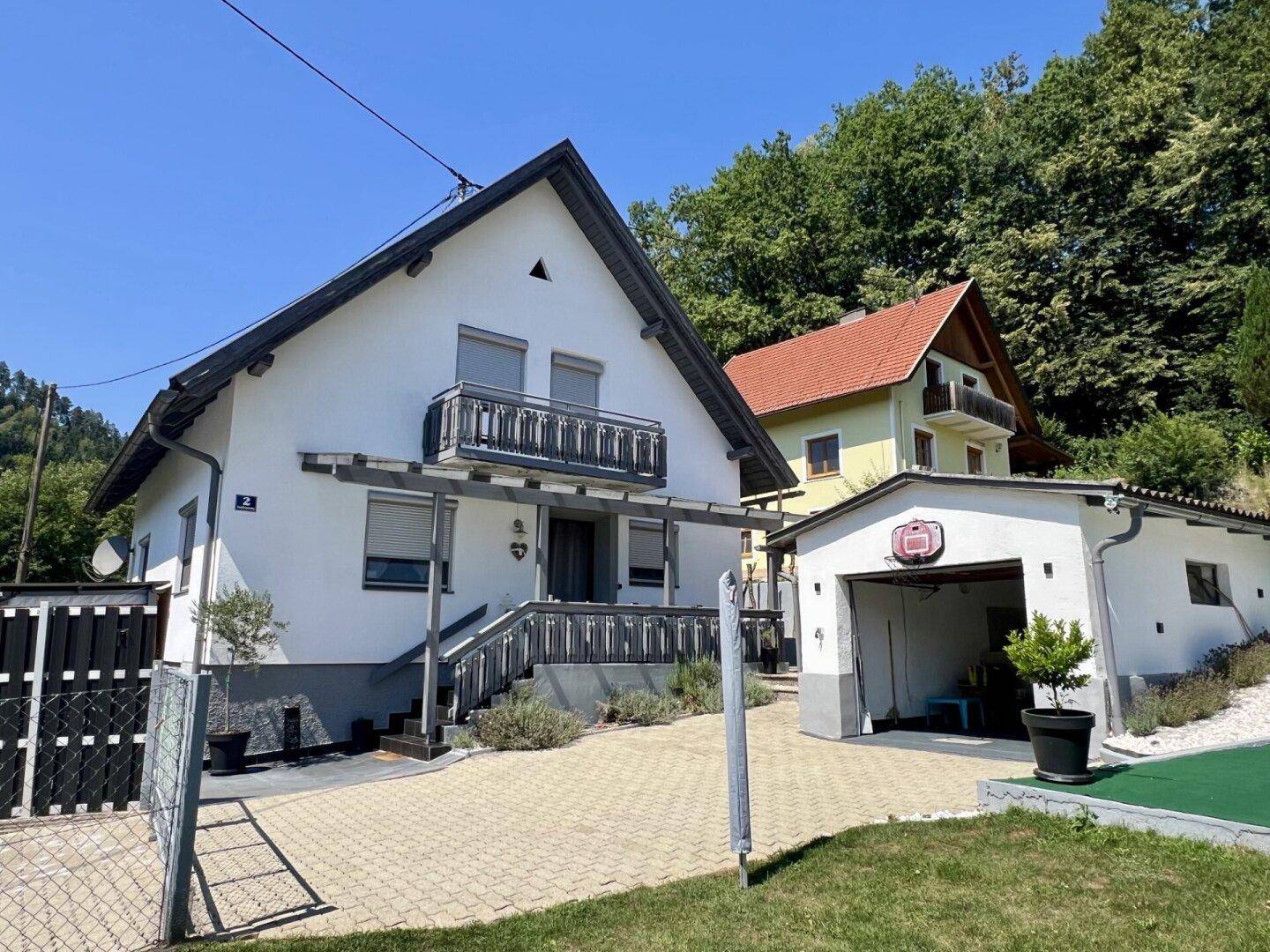 Weißes Einfamilienhaus mit Balkon, Garage und gepflasterter Auffahrt unter blauem Himmel.