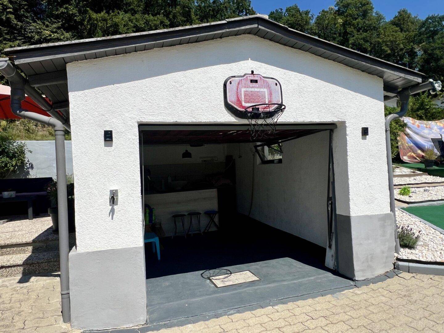 Einzelgarage mit offenem Tor, Basketballkorb und gepflasterter Zufahrt.