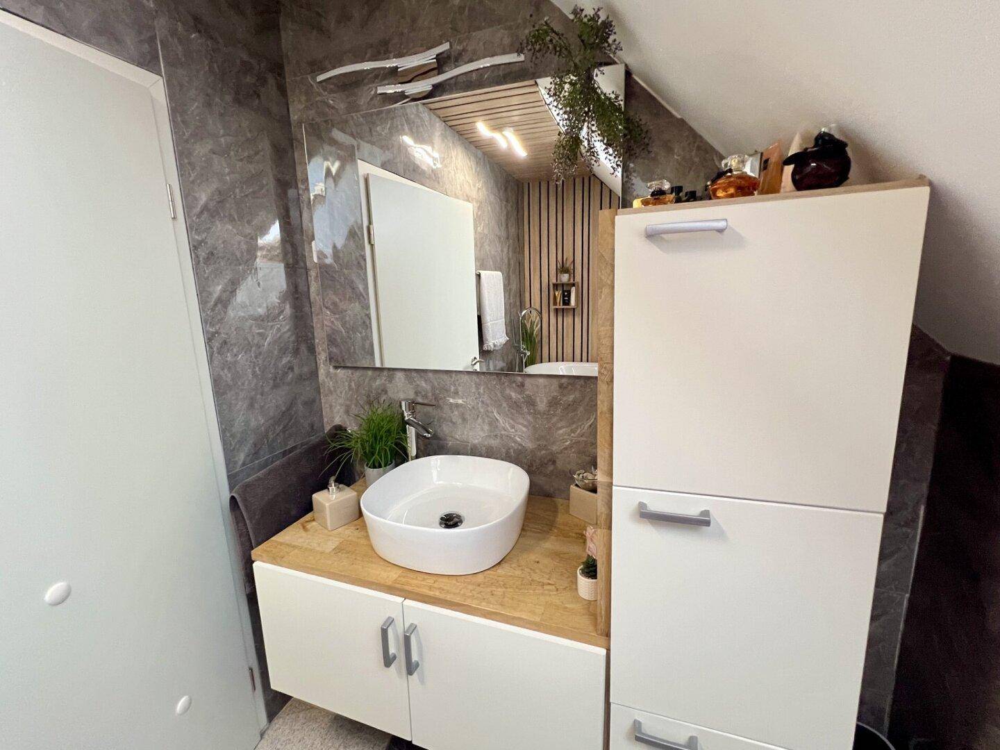 Modernes Badezimmer mit Aufsatzwaschbecken, Spiegelschrank und Holzvertäfelung.
