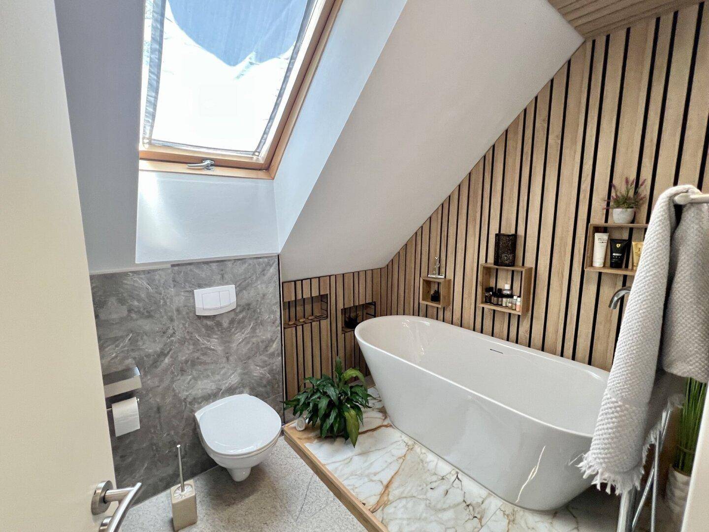 Modernes Badezimmer im Dachgeschoss mit freistehender Badewanne und Dachfenster.