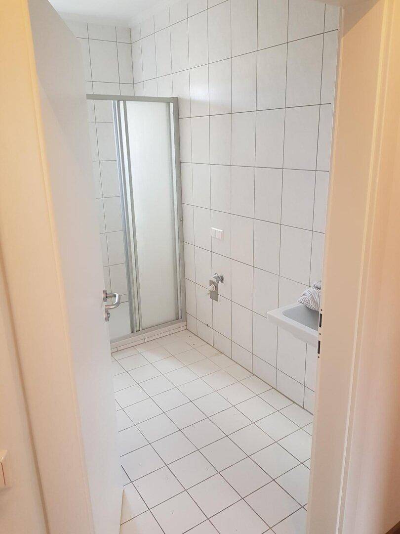 Geräumiges Badezimmer mit weißen Fliesen und einer Duschkabine.