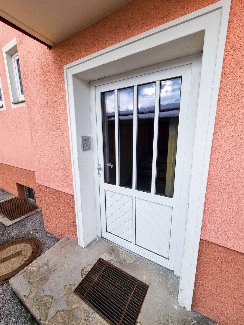 Weiß-verglaste Eingangstür mit seitlicher Gegensprechanlage in einer rosa Fassade.