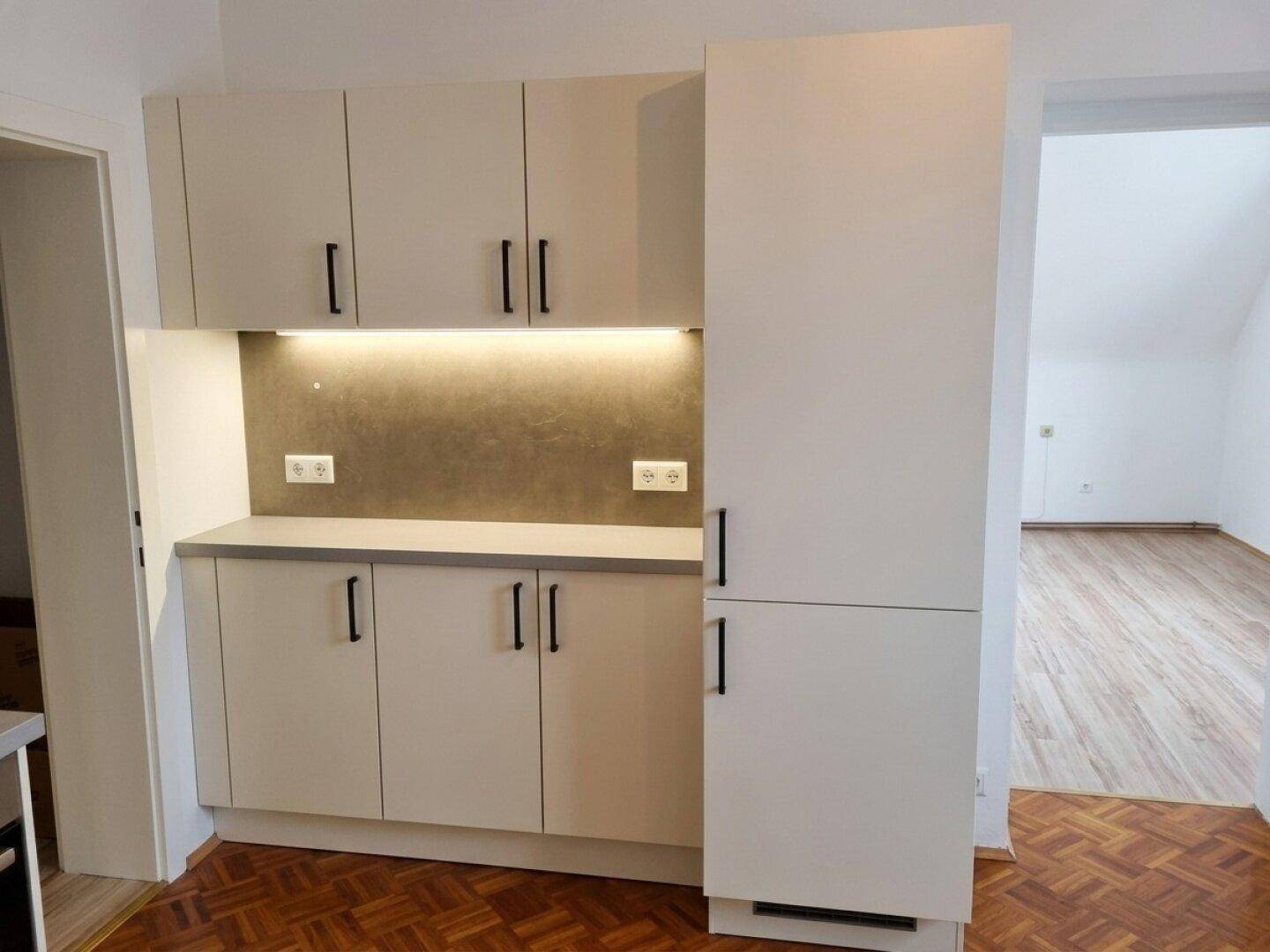 Moderne Küchenzeile in hellem Beige mit Oberschränken und integrierter Beleuchtung.