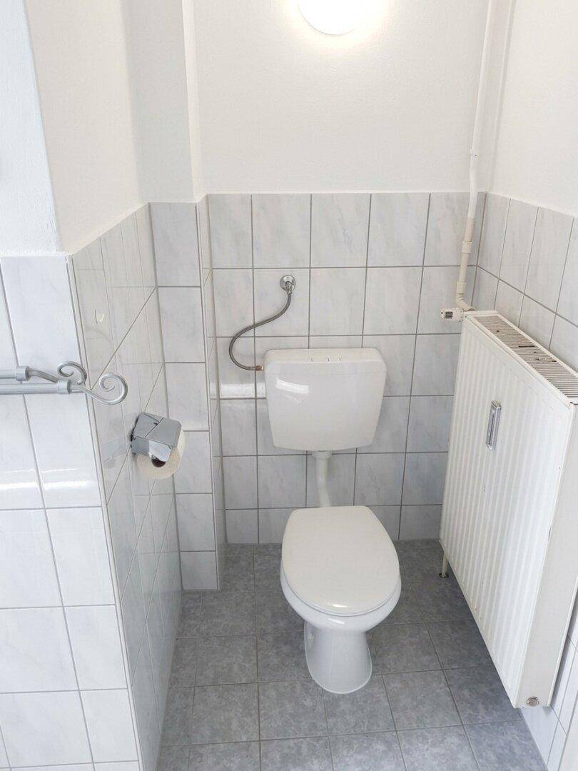 Kleines Gäste-WC mit weißen Fliesen, Toilette und Heizkörper.
