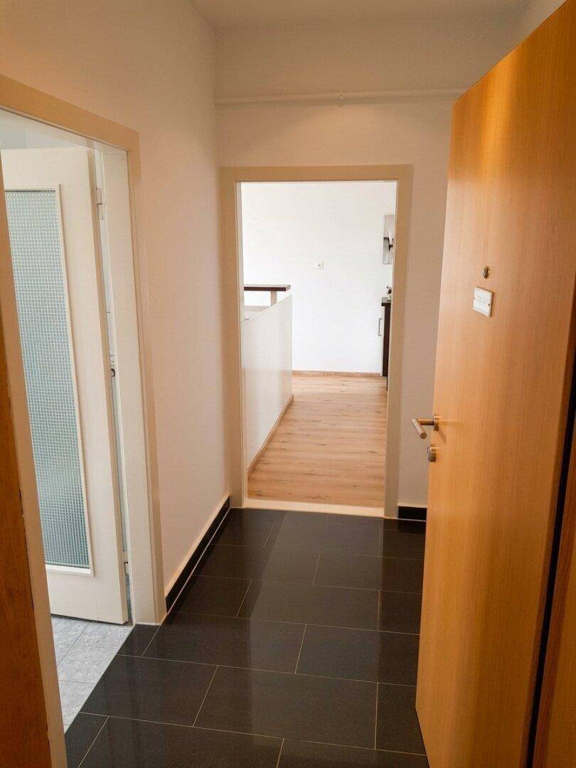Heller Flur mit dunklen Fliesen und Holztüren, der zu weiteren Räumen führt.