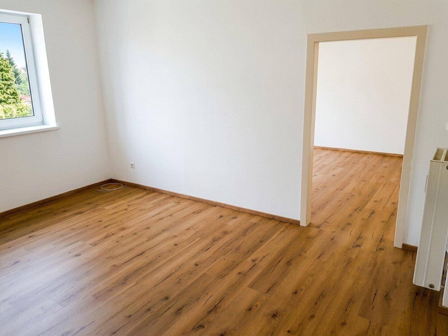 Leeres Zimmer mit hellem Laminatboden und einem Fenster, das viel Licht spendet.
