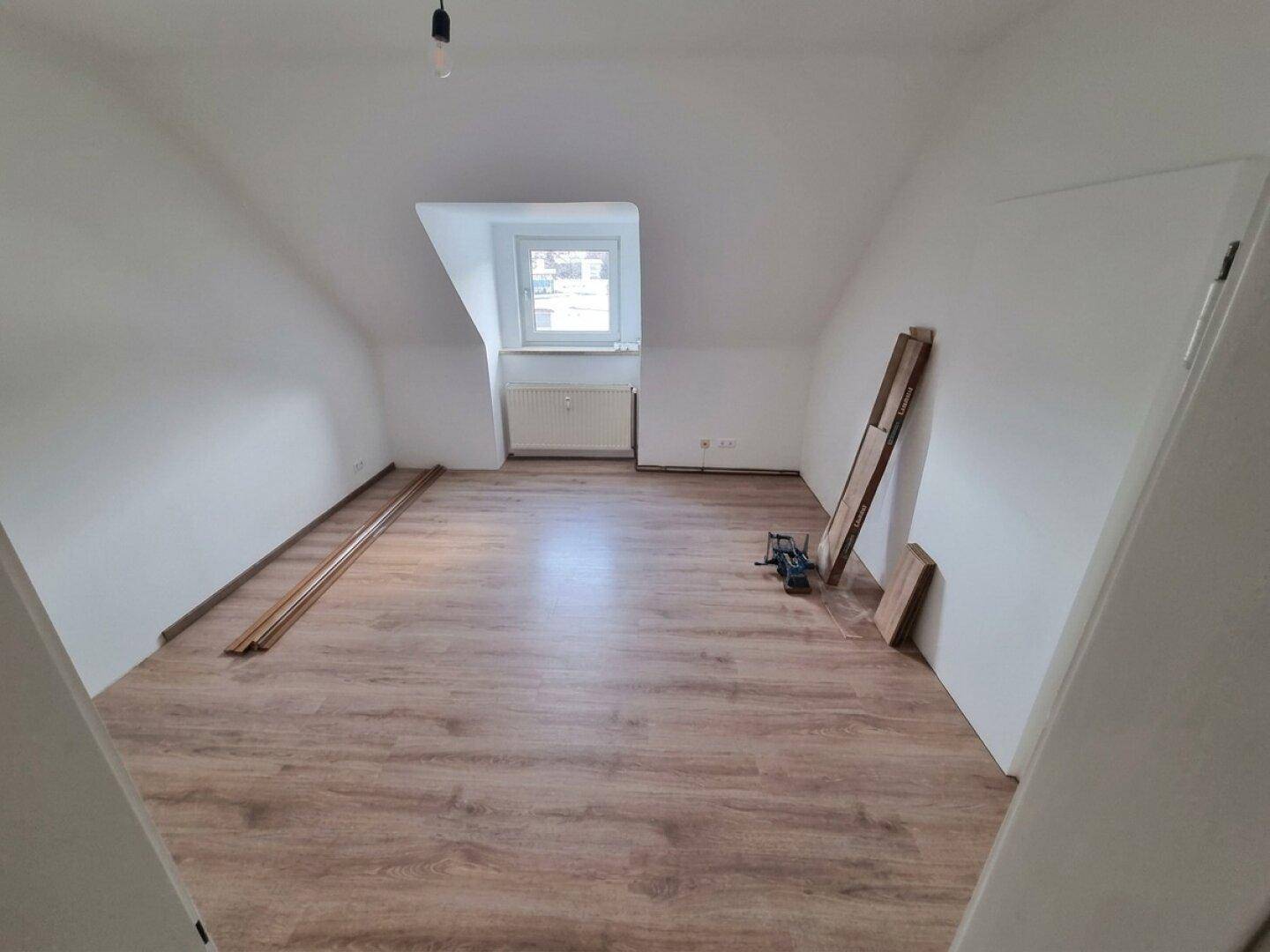 Dachgeschosszimmer mit Laminatboden, schrägen Wänden und Dachfenster.