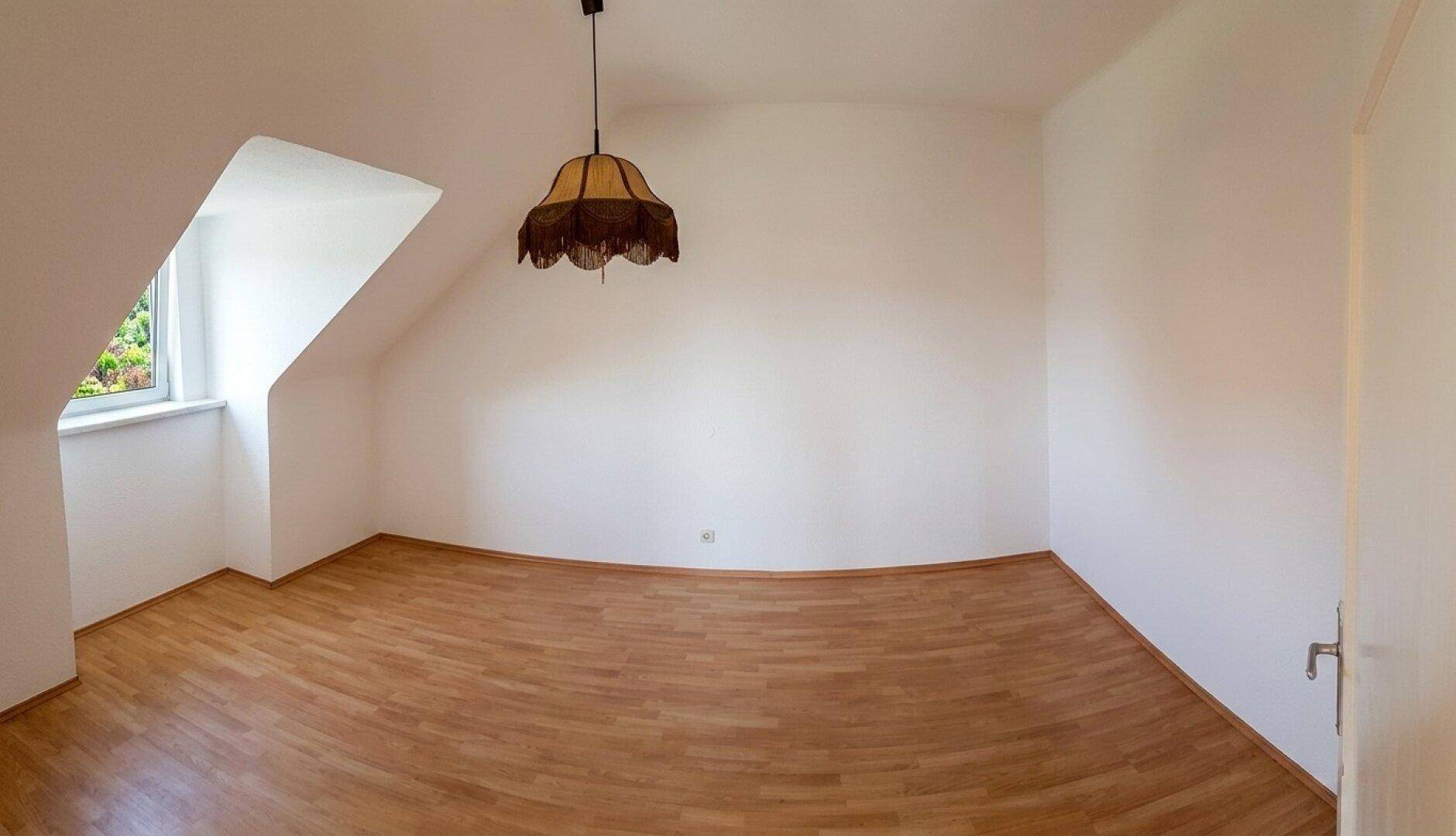 Geräumiges Dachgeschosszimmer mit Laminatboden, schrägen Wänden und Fenster.