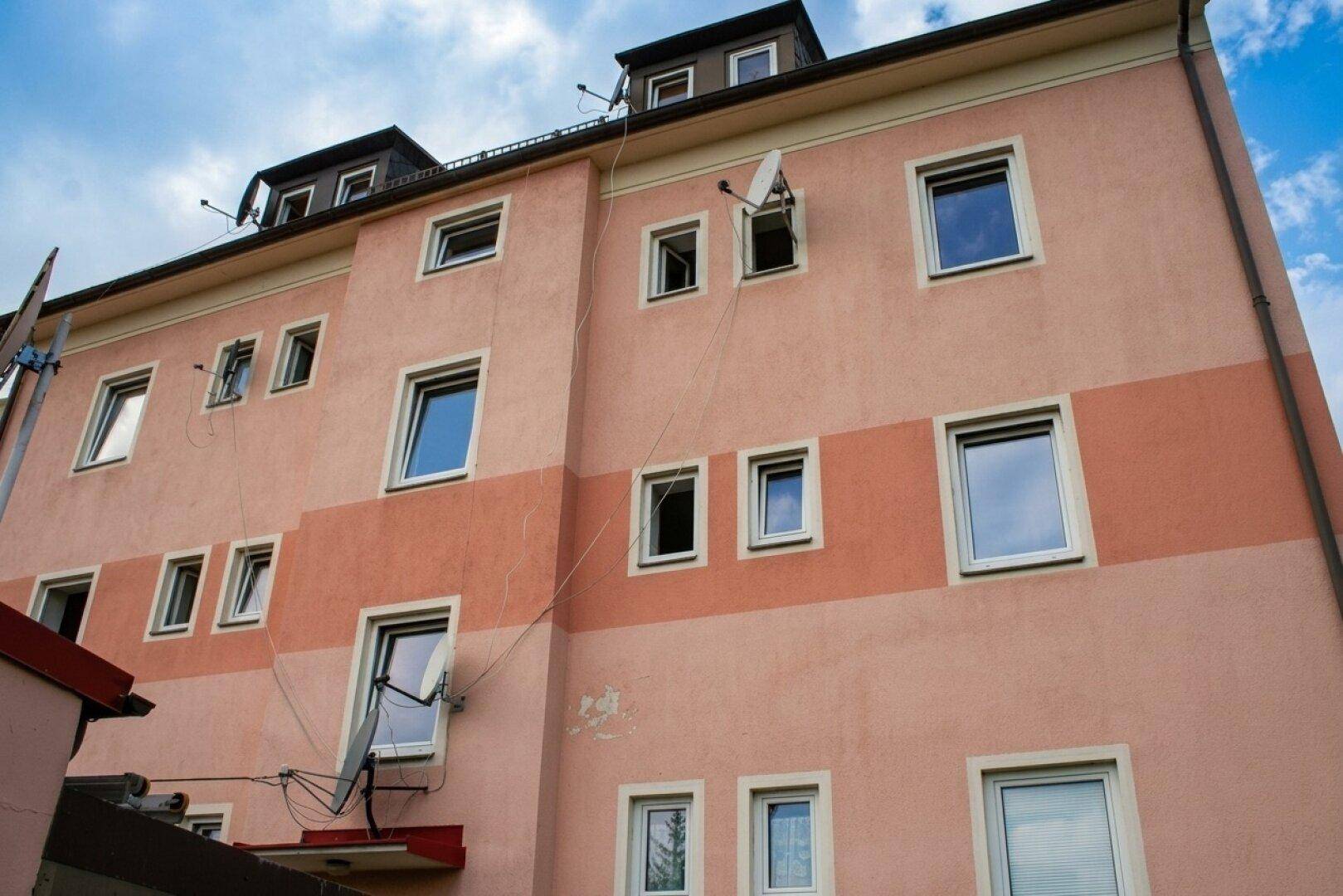 Ansicht der Rückseite eines rosa Mehrfamilienhauses mit mehreren Fenstern und Satellitenschüsseln.