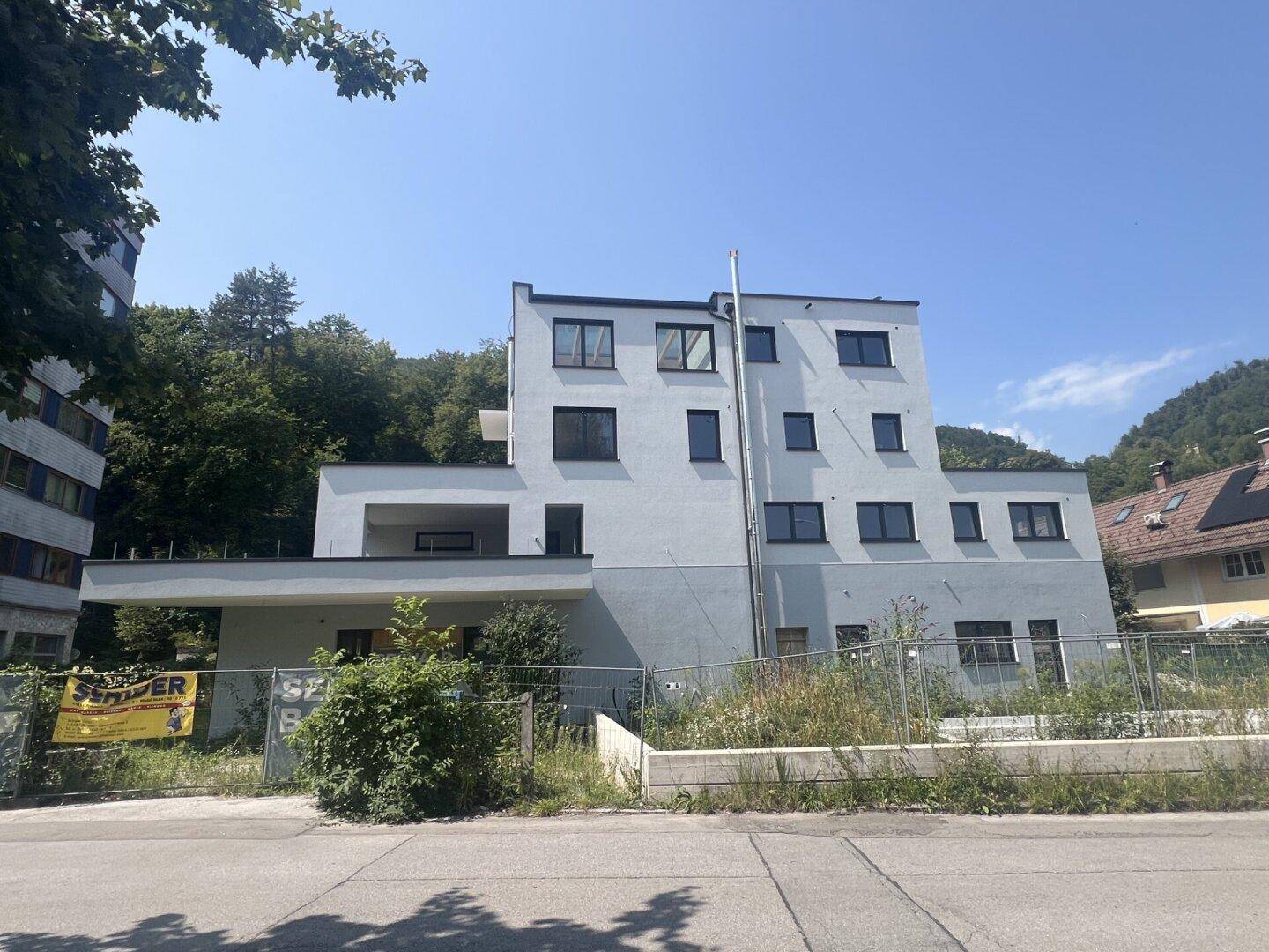 Vorderansicht eines modernen Neubaus mit weißer Fassade und umgebender grüner Landschaft.