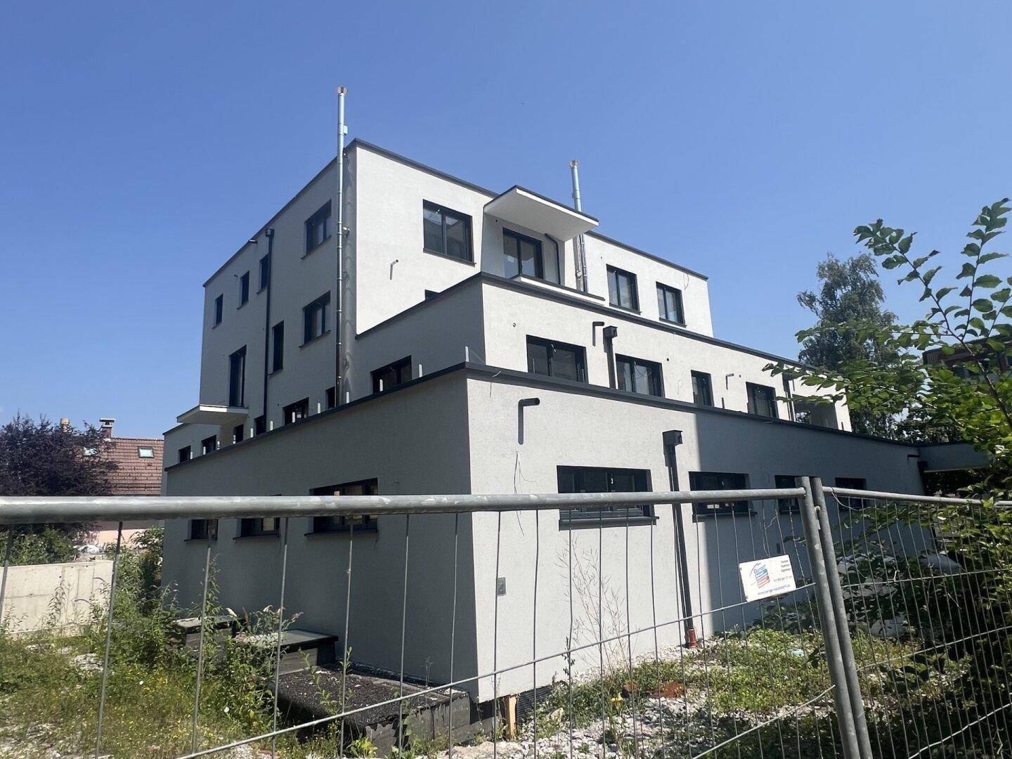 Blick auf die Rückseite eines modernen Neubaus mit grauer Fassade und Flachdächern.