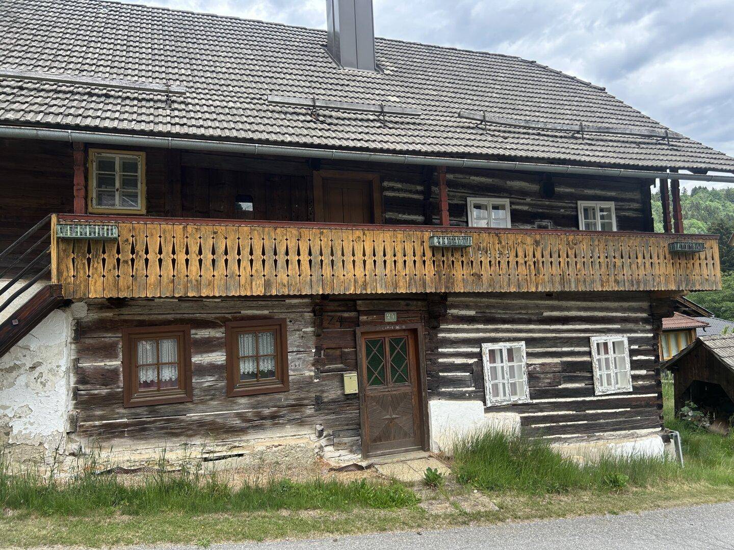 Traditionelles Holzhaus mit Holzbalkon und rotem Ziegeldach, umgeben von grüner Natur und Bäumen.