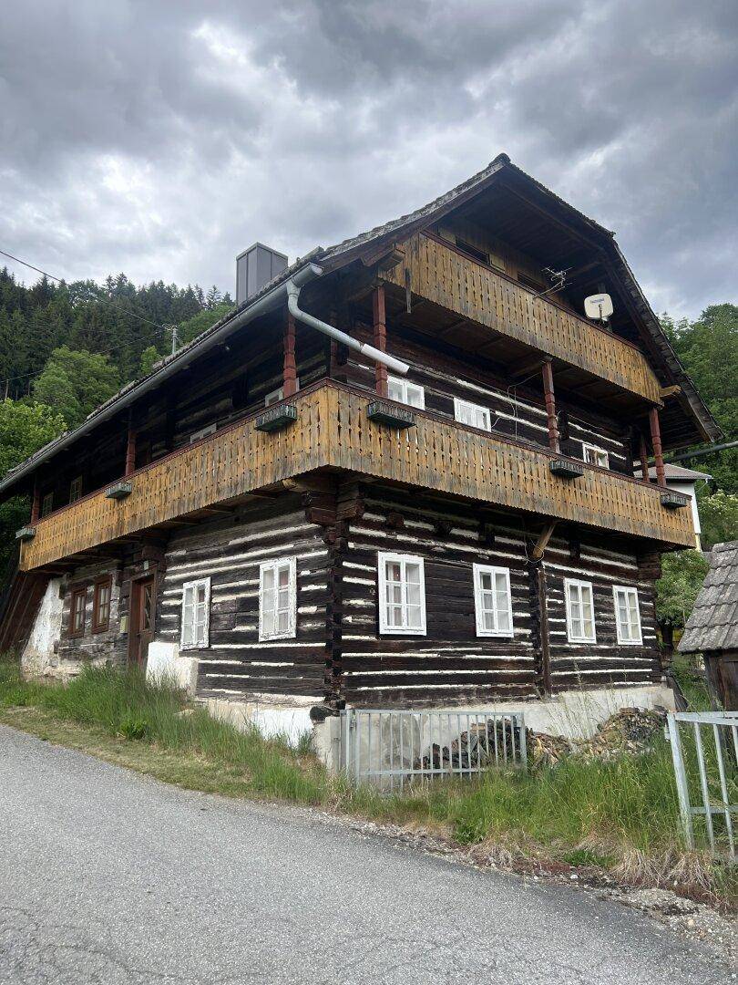 Rustikales Holzhaus mit mehreren Balkonen und Satteldach, umgeben von Bäumen und ländlicher Idylle.