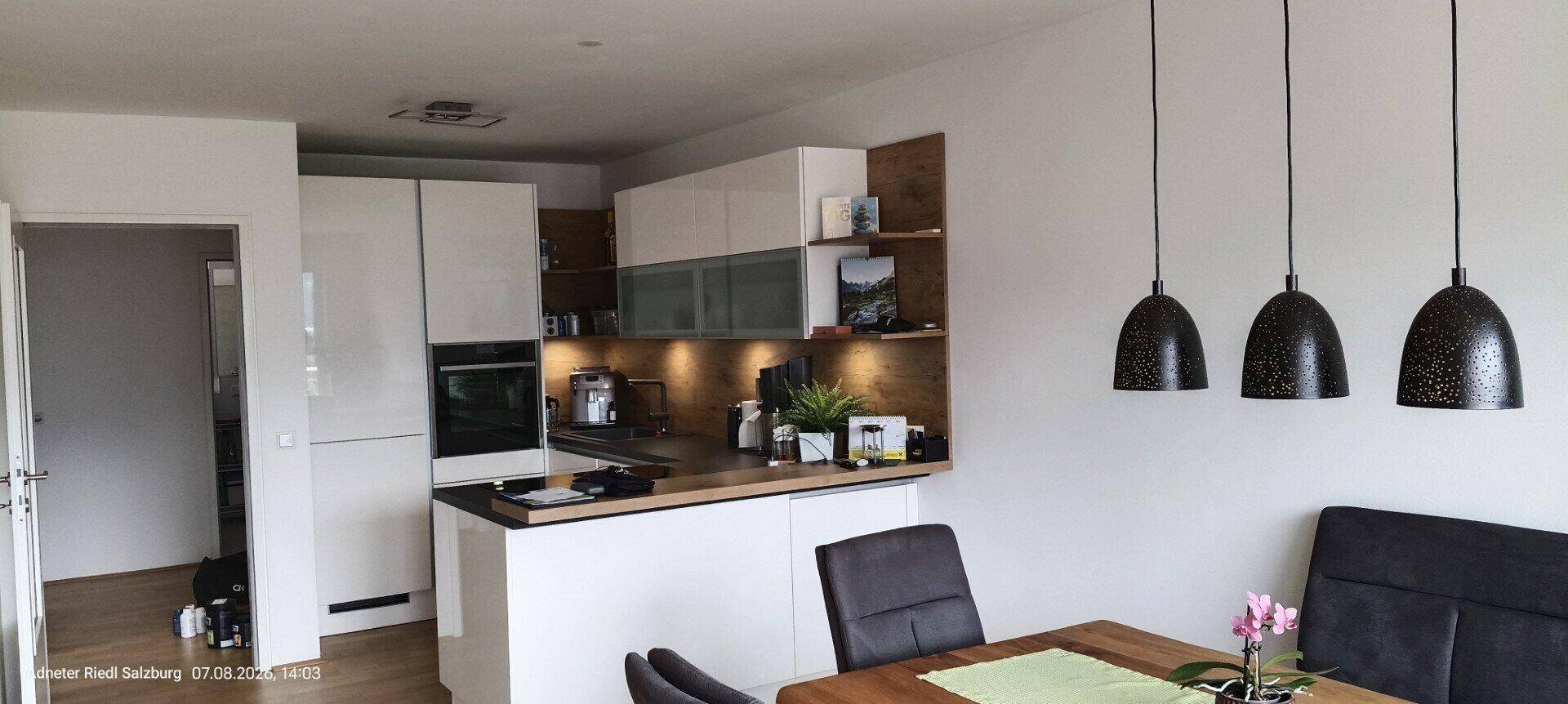 Moderne Einbauküche mit weißen Hochglanzfronten, Holzdetails und integrierten Geräten.