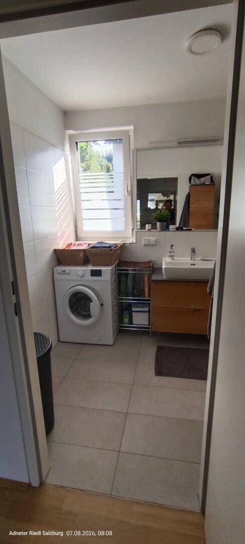 Helles Badezimmer mit Waschmaschine, Einzelwaschbecken und Fenster für Tageslicht.