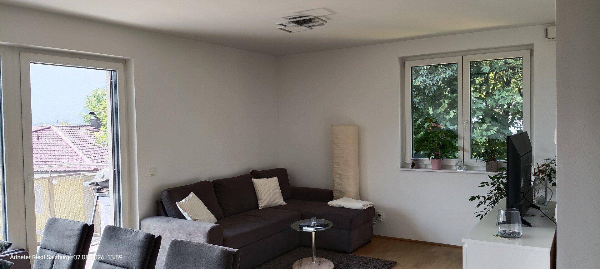 Gemütliches Wohnzimmer mit großem Sofa, Holzboden und Blick ins Grüne.