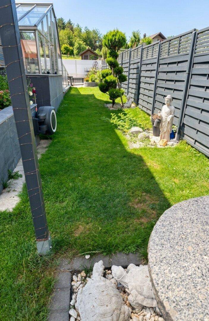 Schmaler Gartenweg mit Rasenfläche, dekorativen Statuen und hohem Sichtschutzzaun.