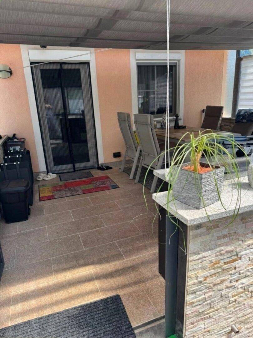 Gemütliche überdachte Terrasse mit Esstisch und Stühlen, ideal für Mahlzeiten im Freien.