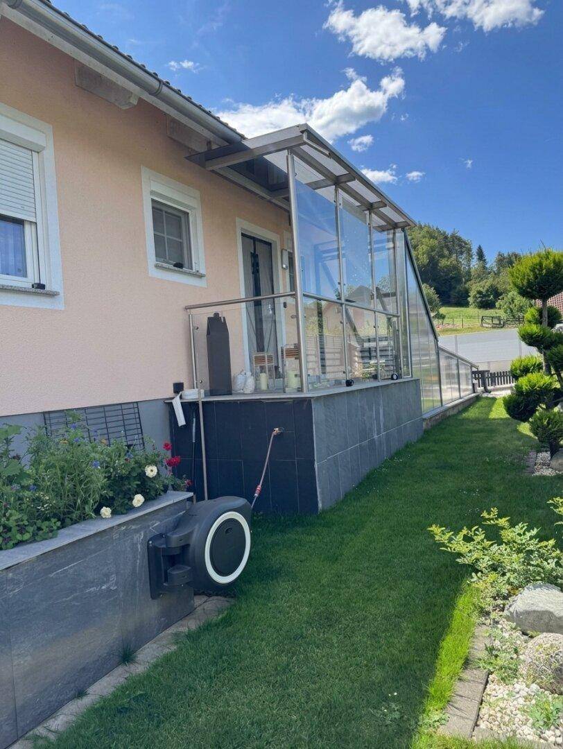 Seitenansicht des Hauses mit Glasanbau, Rasenfläche und gepflegter Bepflanzung.