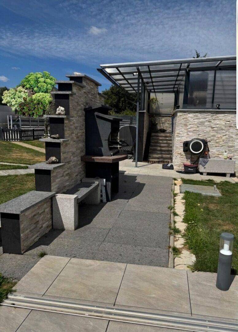 Außenbereich mit gemauertem Grillplatz und Steinfliesen, angrenzend an das Gebäude.