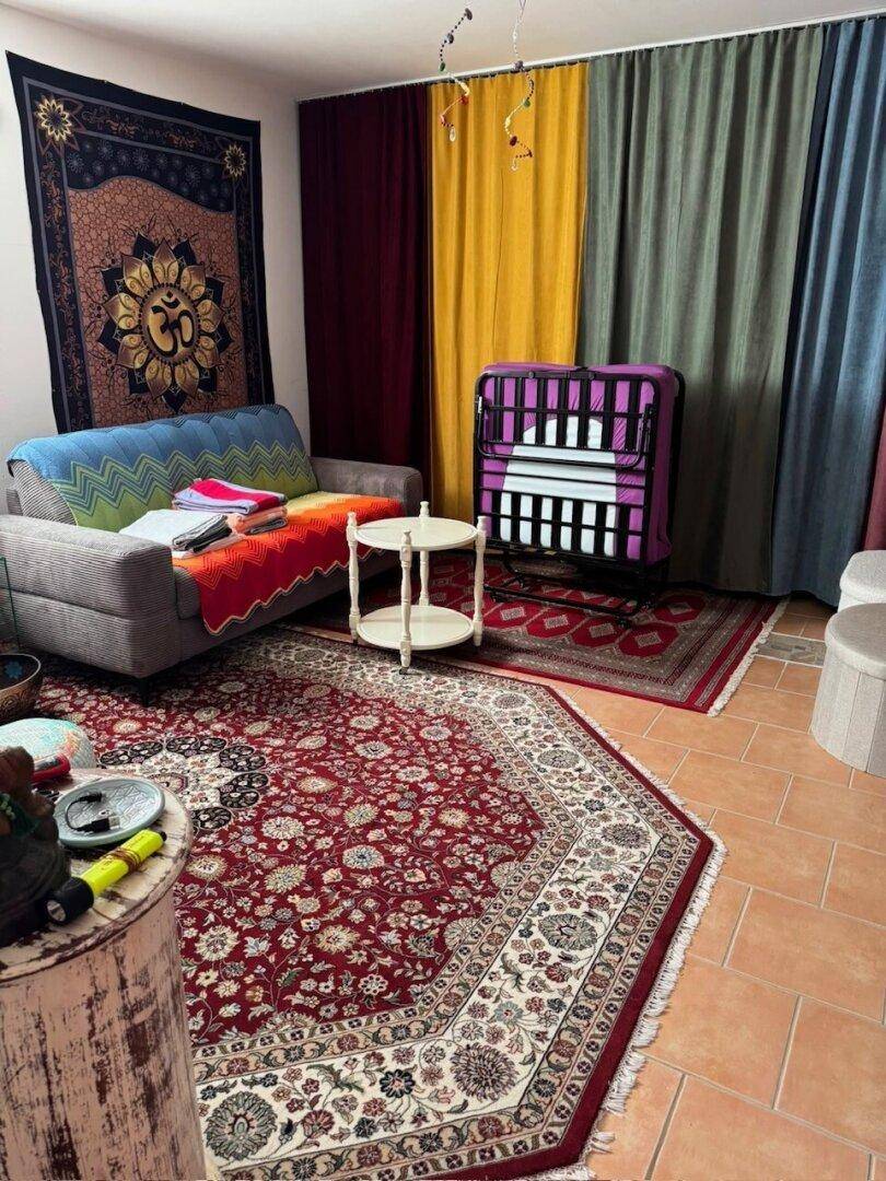 Gemütliches Wohnzimmer mit Sofa, bunten Teppichen und dekorativen Wandbehängen.