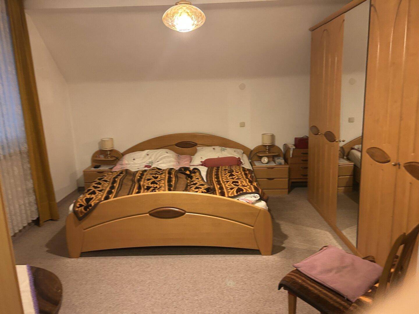 Gemütliches Schlafzimmer mit Holzmöbeln, Teppichboden und Dachschräge, ausgestattet mit einem großen Kleiderschrank.