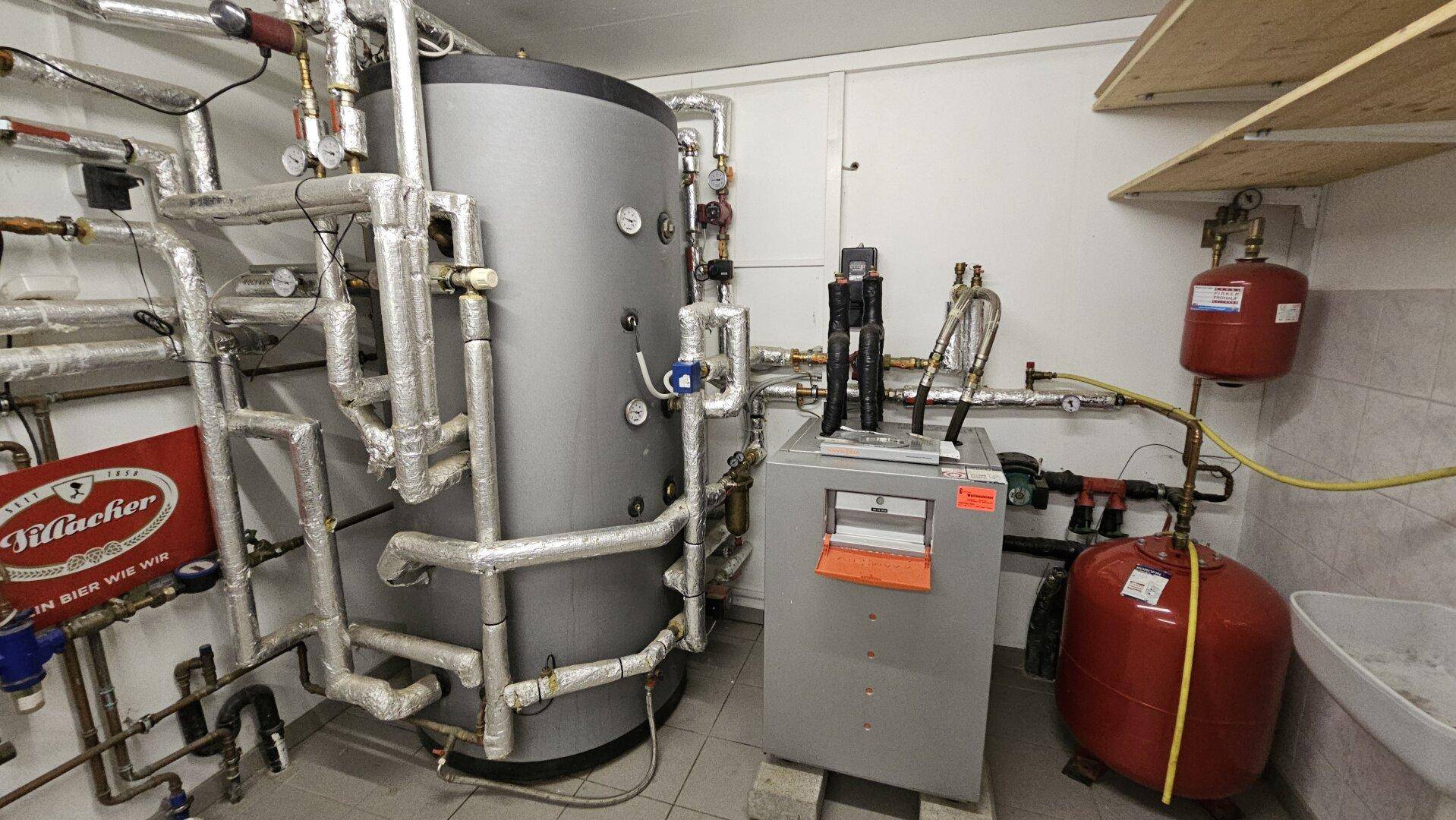 Technikraum mit großem Warmwasserspeicher, komplexen Rohrleitungen und Heizungsanlagen.