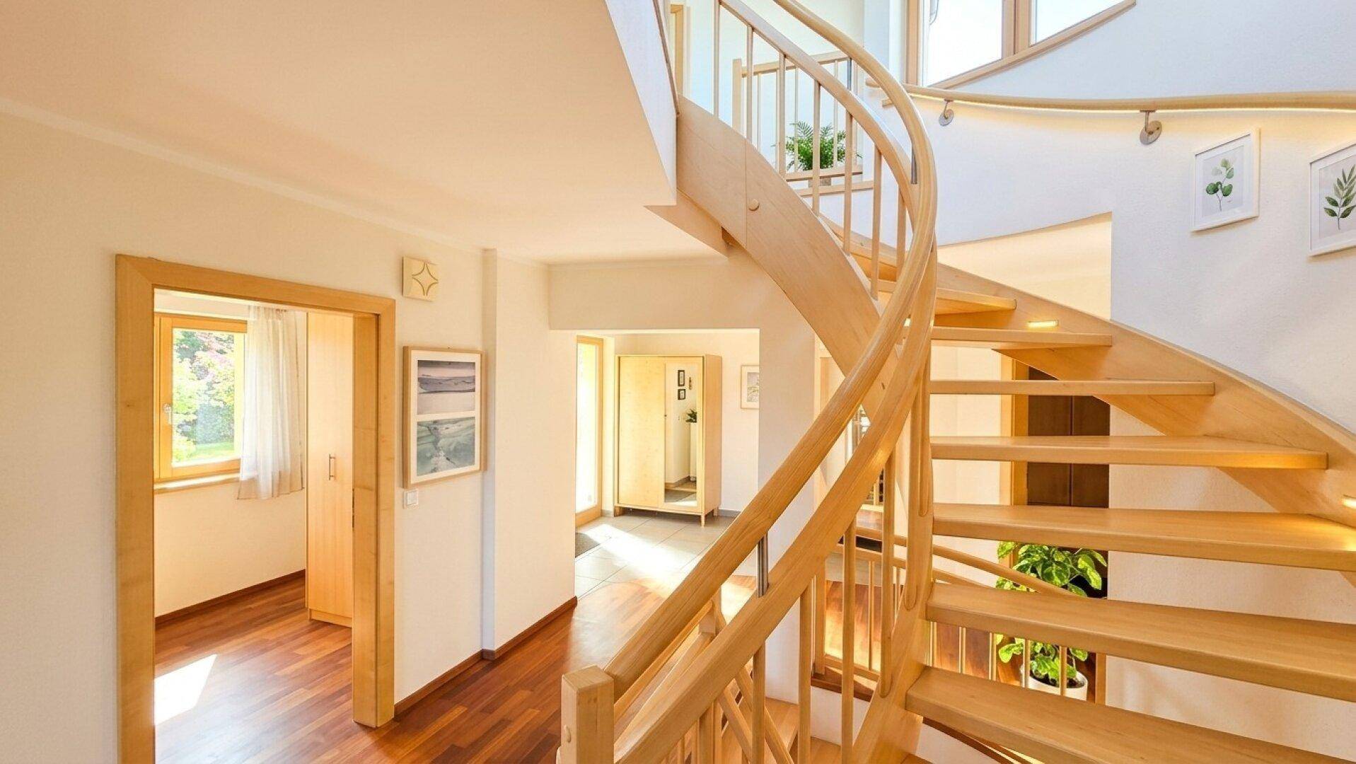 Heller Flur mit eleganter Holzwendeltreppe und hochwertigem Parkettboden, der zum Obergeschoss führt.